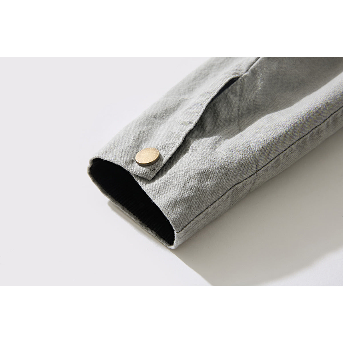 Close-up of a light gray jacket sleeve cuff with black lining and a brass snap tab.