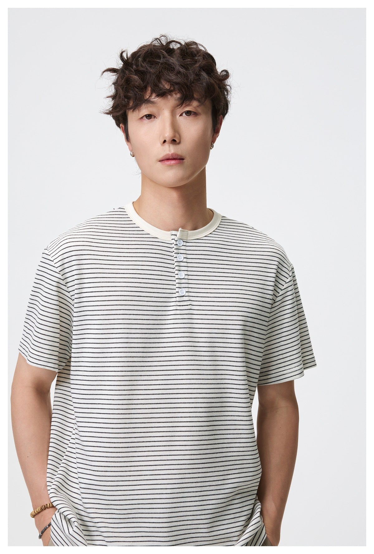 Close view of an ivory T-shirt with thin black stripes, a contrast crew neck, and a short button placket, worn by a model.