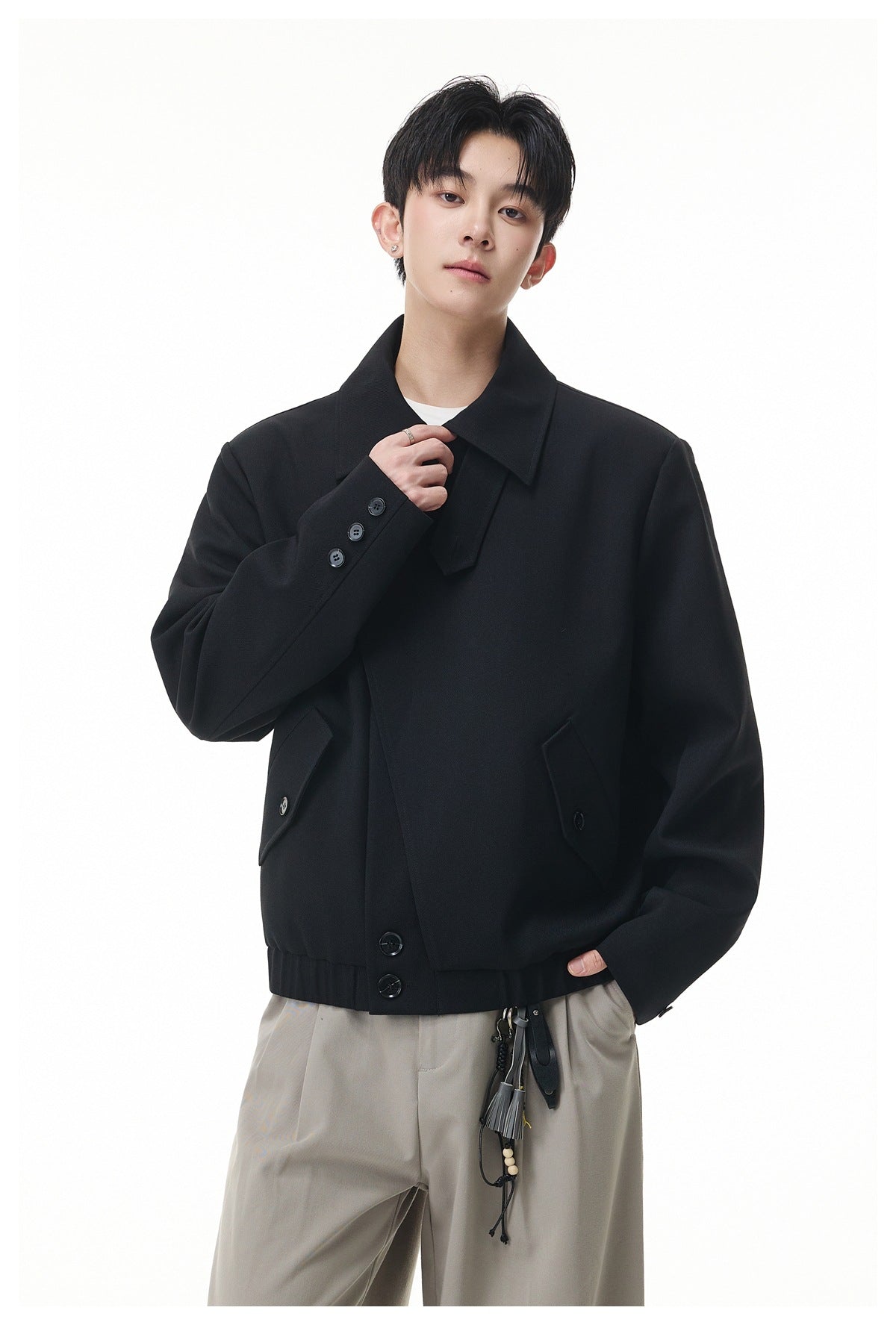 Model wearing a black jacket with a wide collar, buttoned cuffs, angled pockets and a ribbed hem.