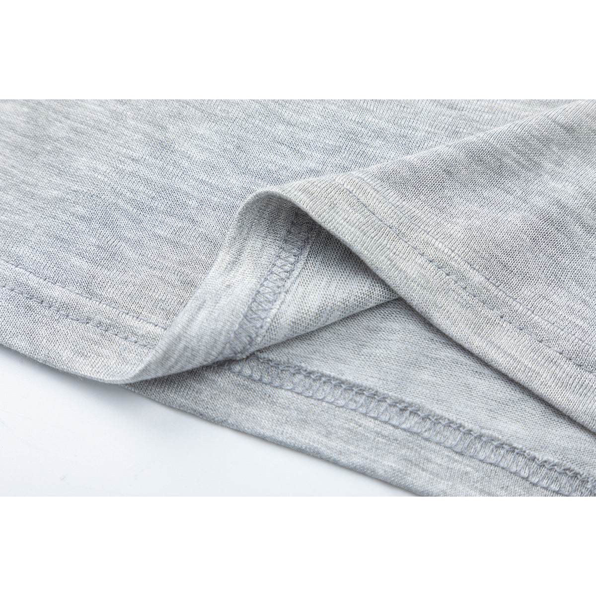 Close-up of the light gray heather shirt's folded hem and visible overlock stitching.