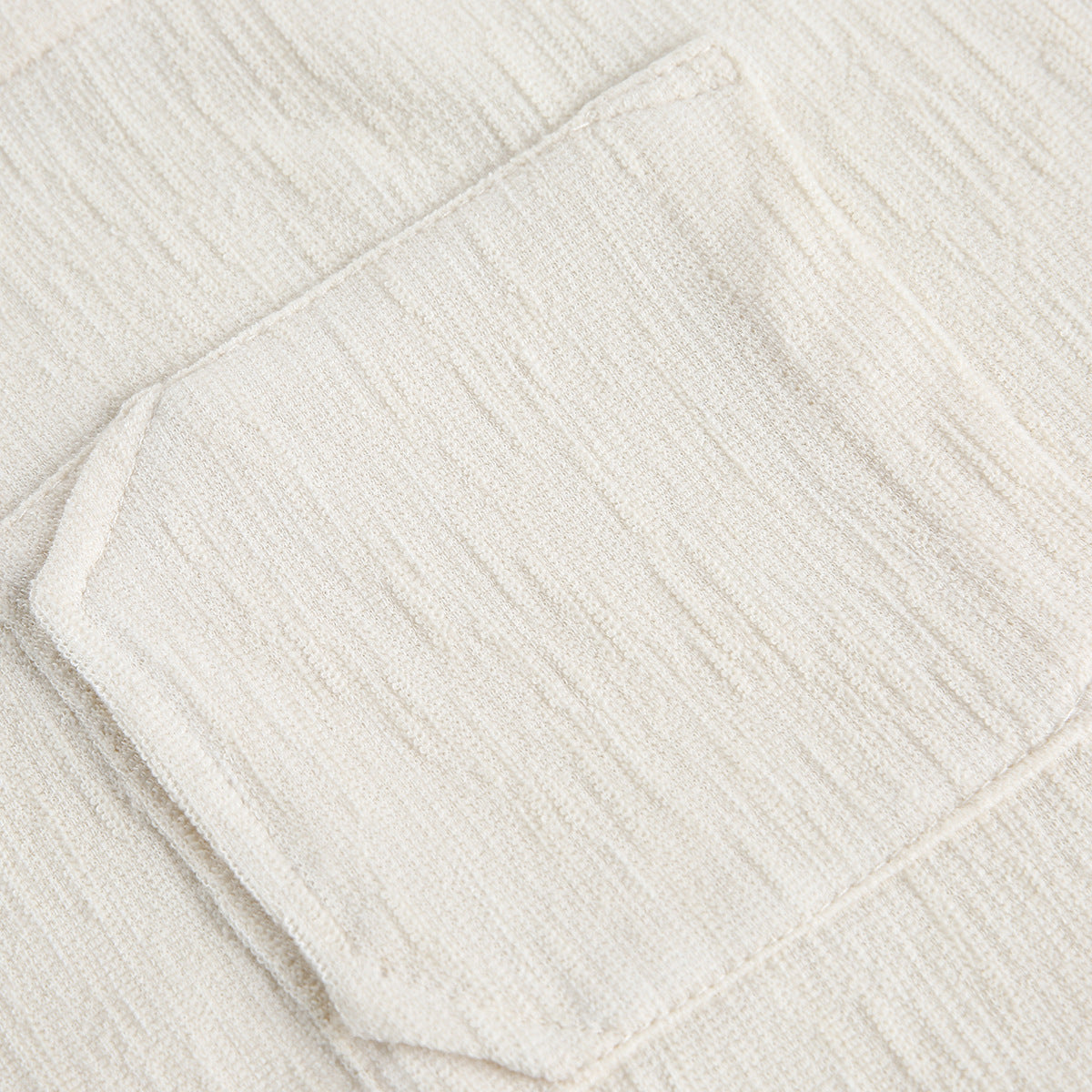 Close-up of a rectangular patch pocket on a cream textured knit shirt.