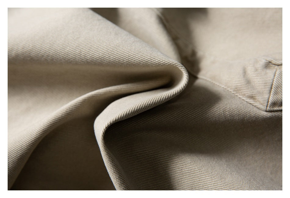 Macro view of beige trouser fabric folded to show its diagonal weave and stitched edge.