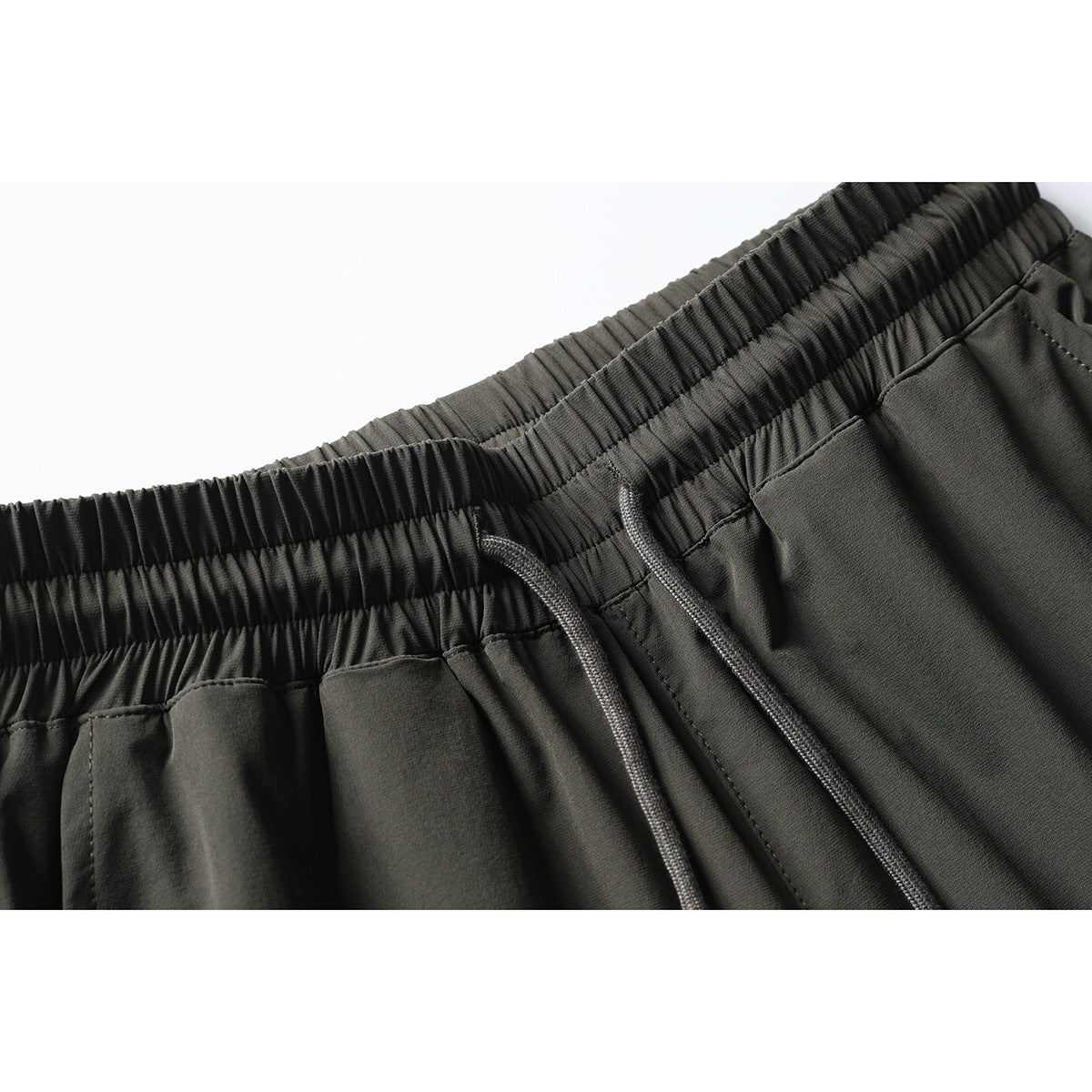 Close-up of dark olive pants with a gathered elastic waistband and matching drawstrings.