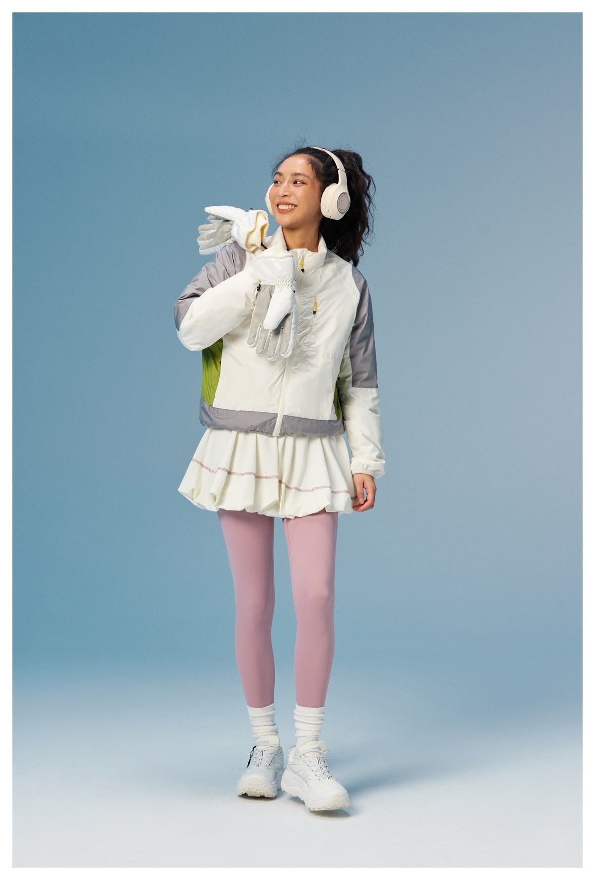 Model wearing a white color-block zip jacket with gray sleeves and a lime side panel, a white skirt, and pink leggings.