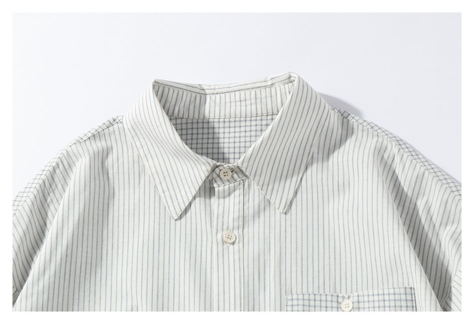Cropped view of an off-white shirt's gray-striped front, pointed collar, buttons, and checked inner yoke.