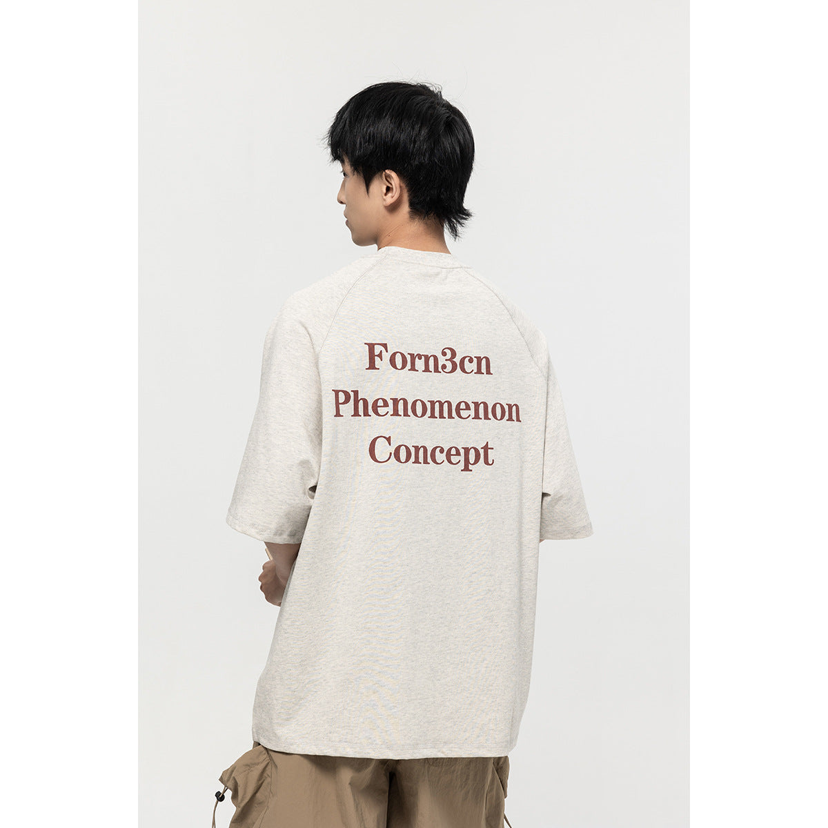 Model viewed from behind wearing an off-white T-shirt with large burgundy back lettering.