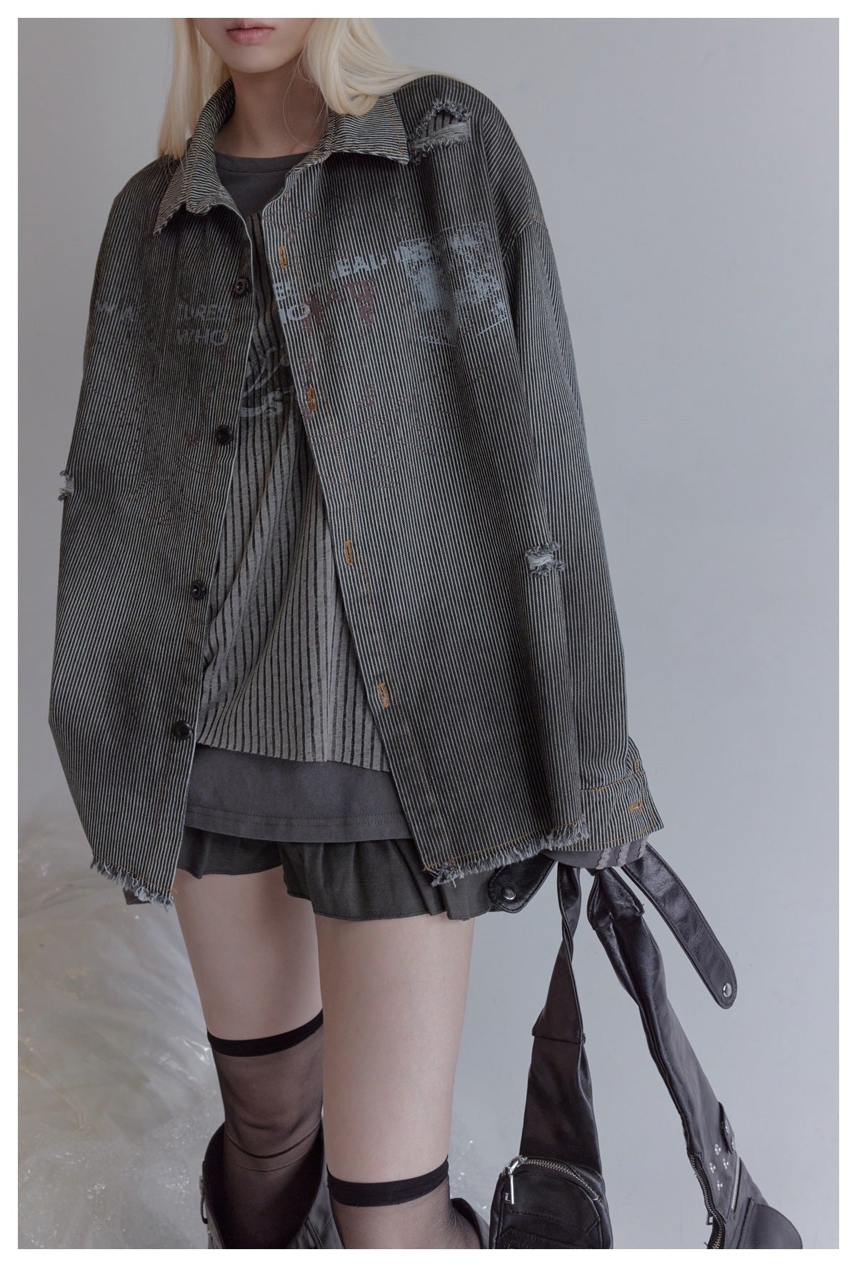 Close view of a model wearing a charcoal pinstriped jacket with distressed patches and frayed edges.