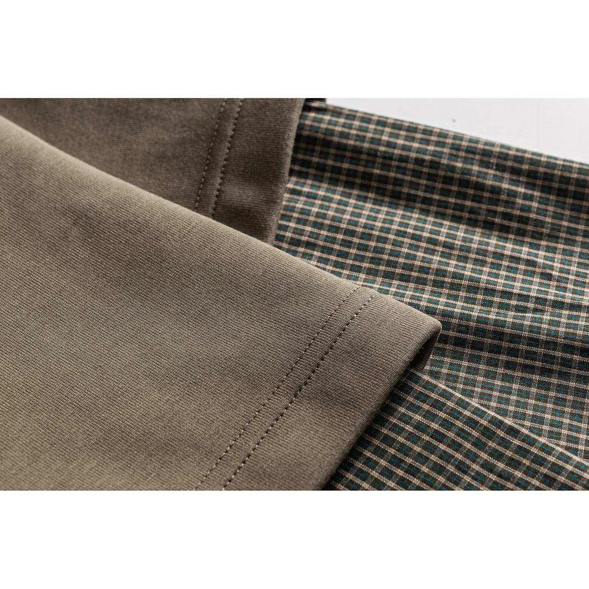Close-up of taupe fabric with a double-stitched seam beside brown and teal plaid fabric.