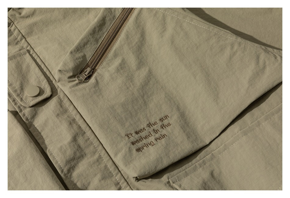 Close-up of a khaki jacket with a diagonal zipper, snap tab, and small embroidered English text.