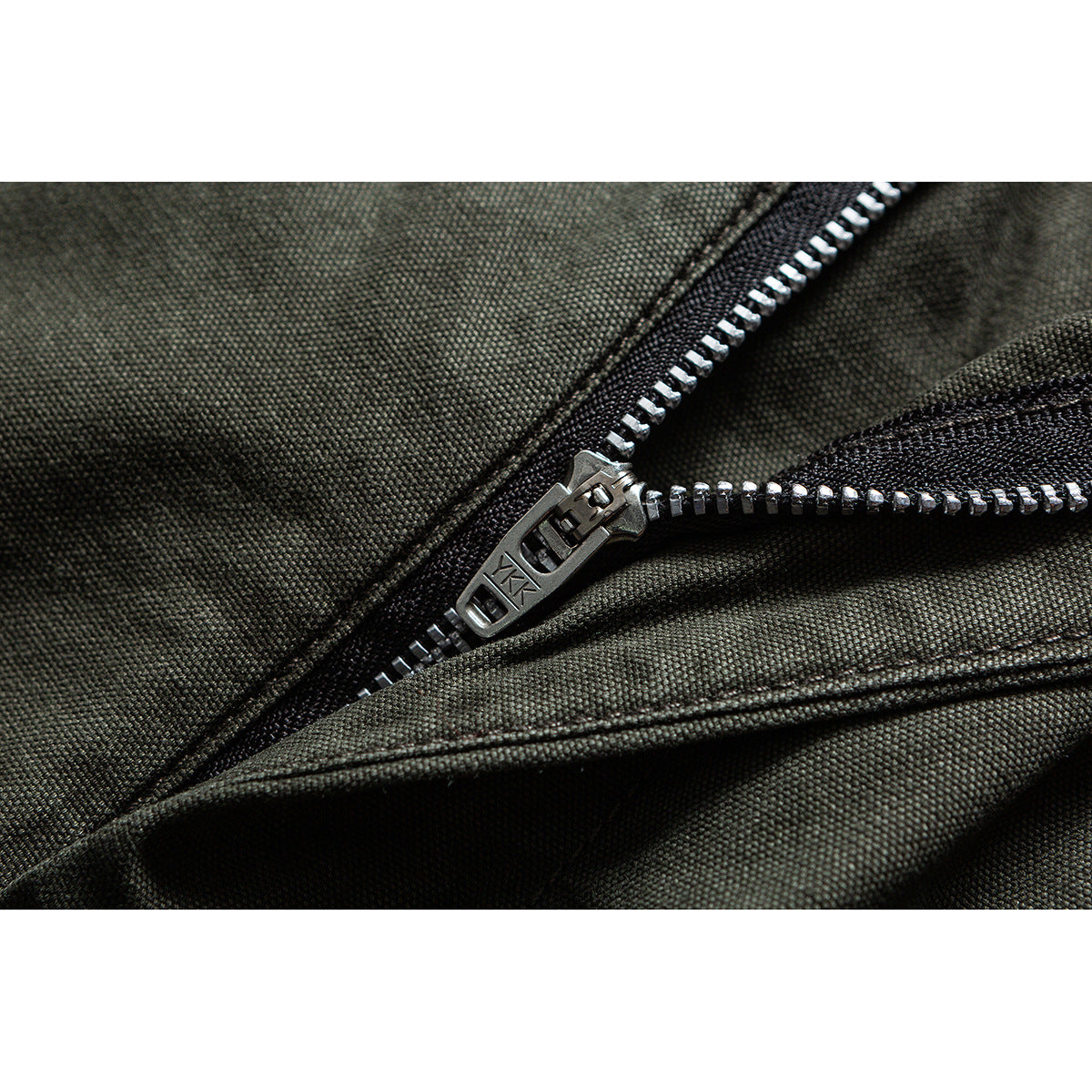Close-up of a metal zipper and pull on dark olive fabric; the pull is marked YKK.