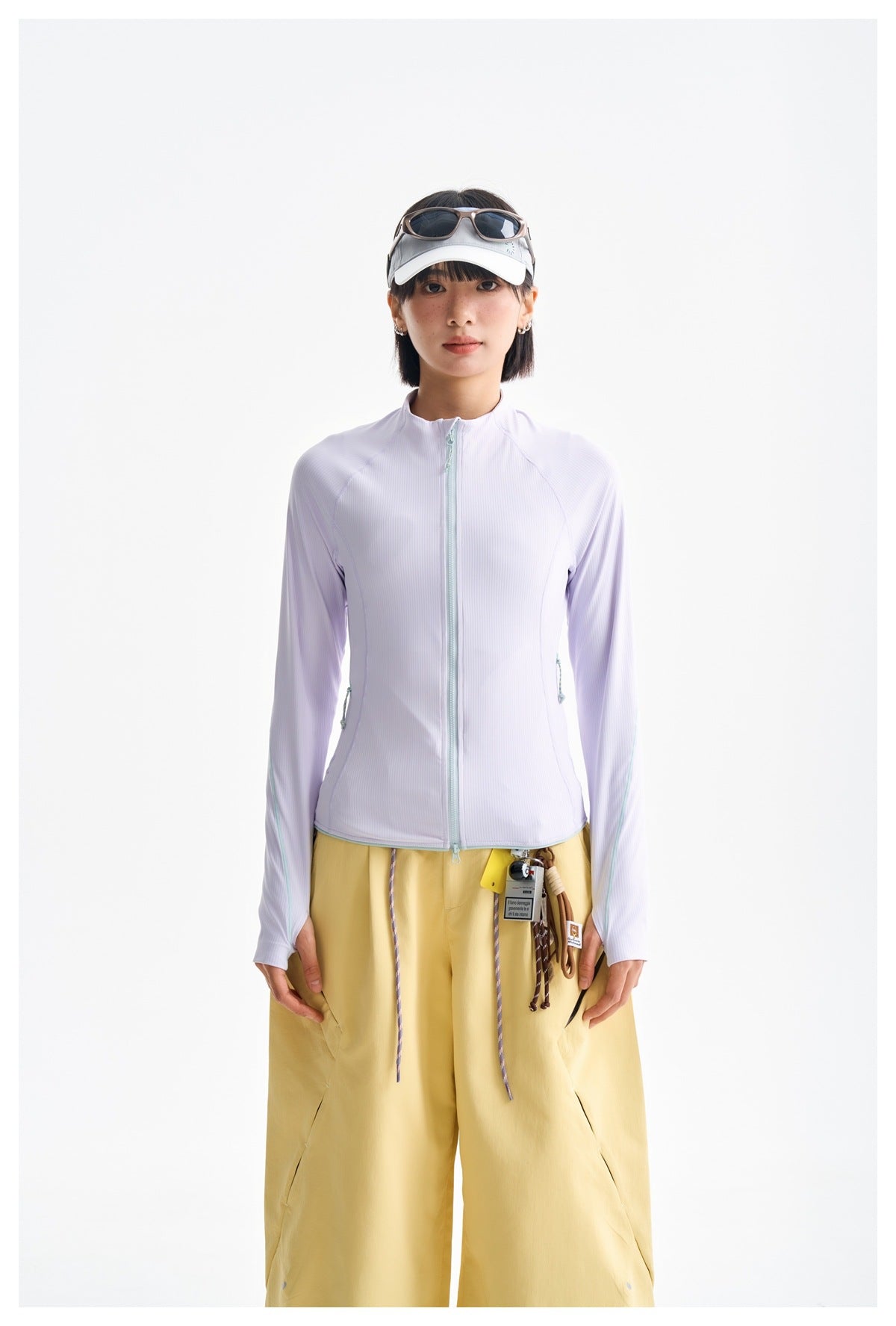 Front view of a model wearing a pale lavender zip-front jacket with mint trim and loose mustard-yellow trousers.