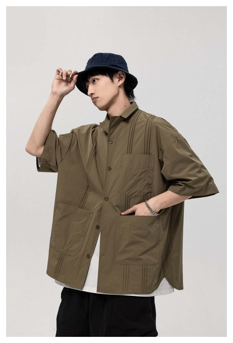 Model wearing an olive-brown short-sleeve button-up shirt with three front pockets and vertical stitched details.