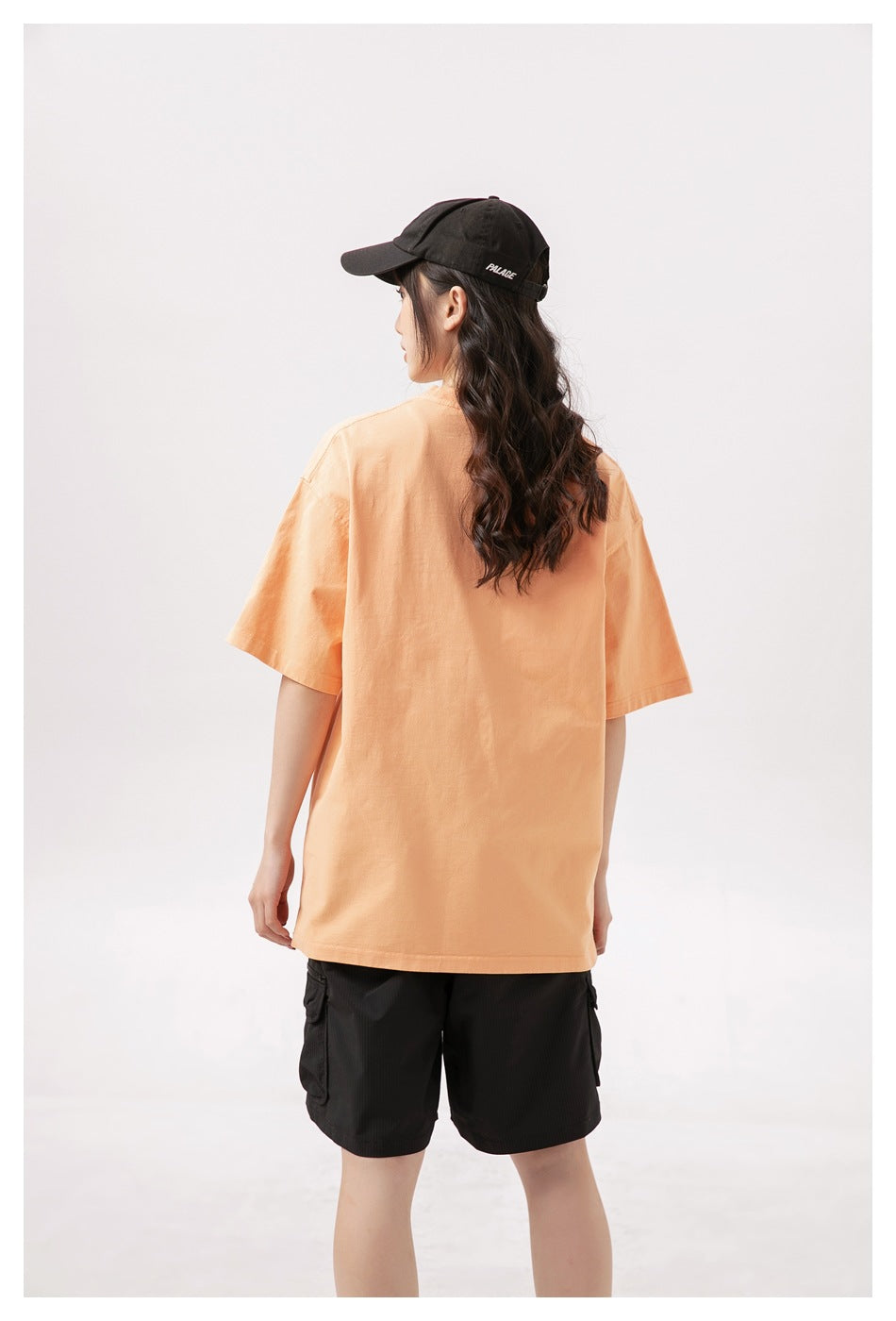 Back view of a model wearing an oversized peach T-shirt and black cargo shorts.