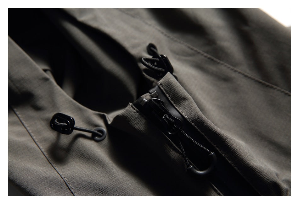 Close-up of dark gray jacket fabric with black zipper pulls and cord loops.