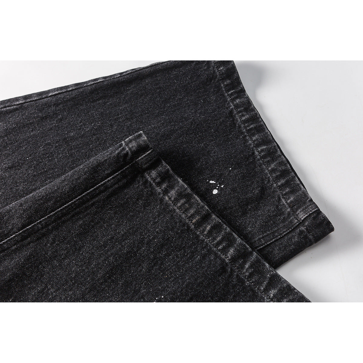 Close-up of black washed trouser legs showing the folded hems and small white paint splatters.