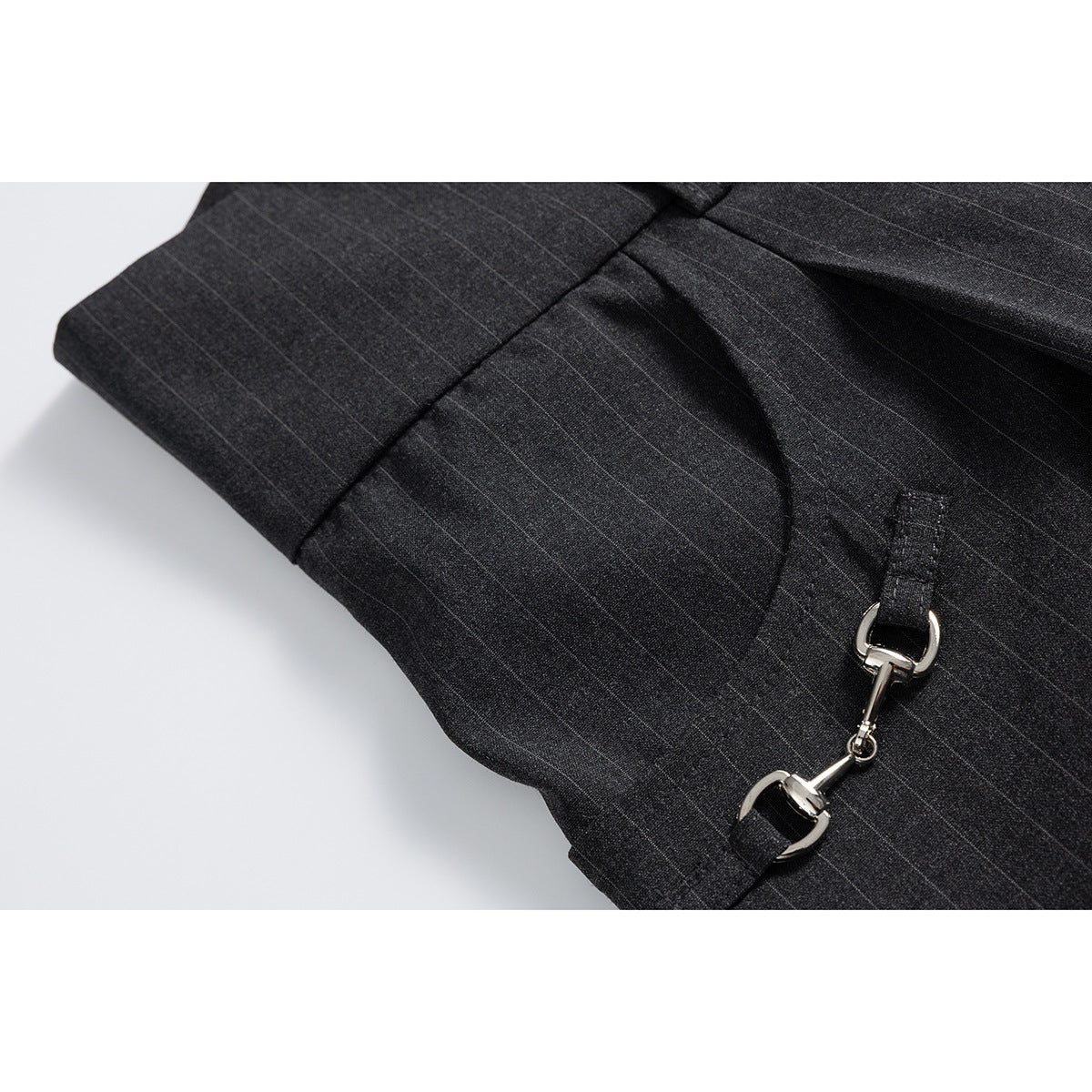 Close-up of charcoal pinstripe trousers showing a curved pocket and polished silver hardware.