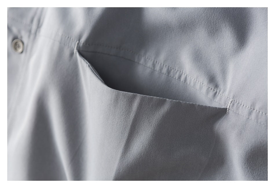 Close-up of a light gray shirt's stitched chest pocket and a nearby button.