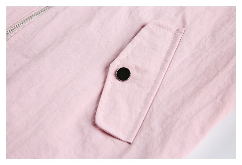Close-up of a pale pink jacket pocket flap with a dark snap button and part of the zipper.