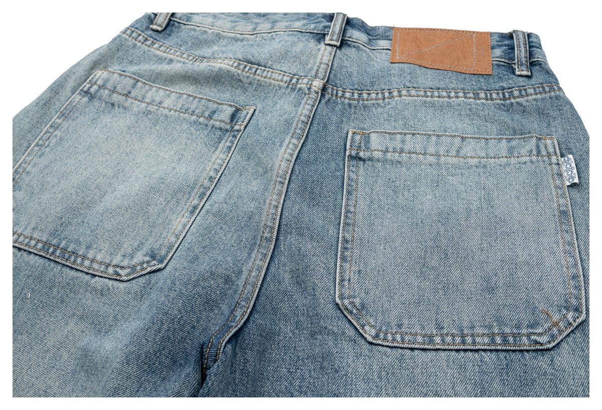 Close view of the back of light-wash denim jeans, showing two rear pockets, belt loops and a tan waistband patch.