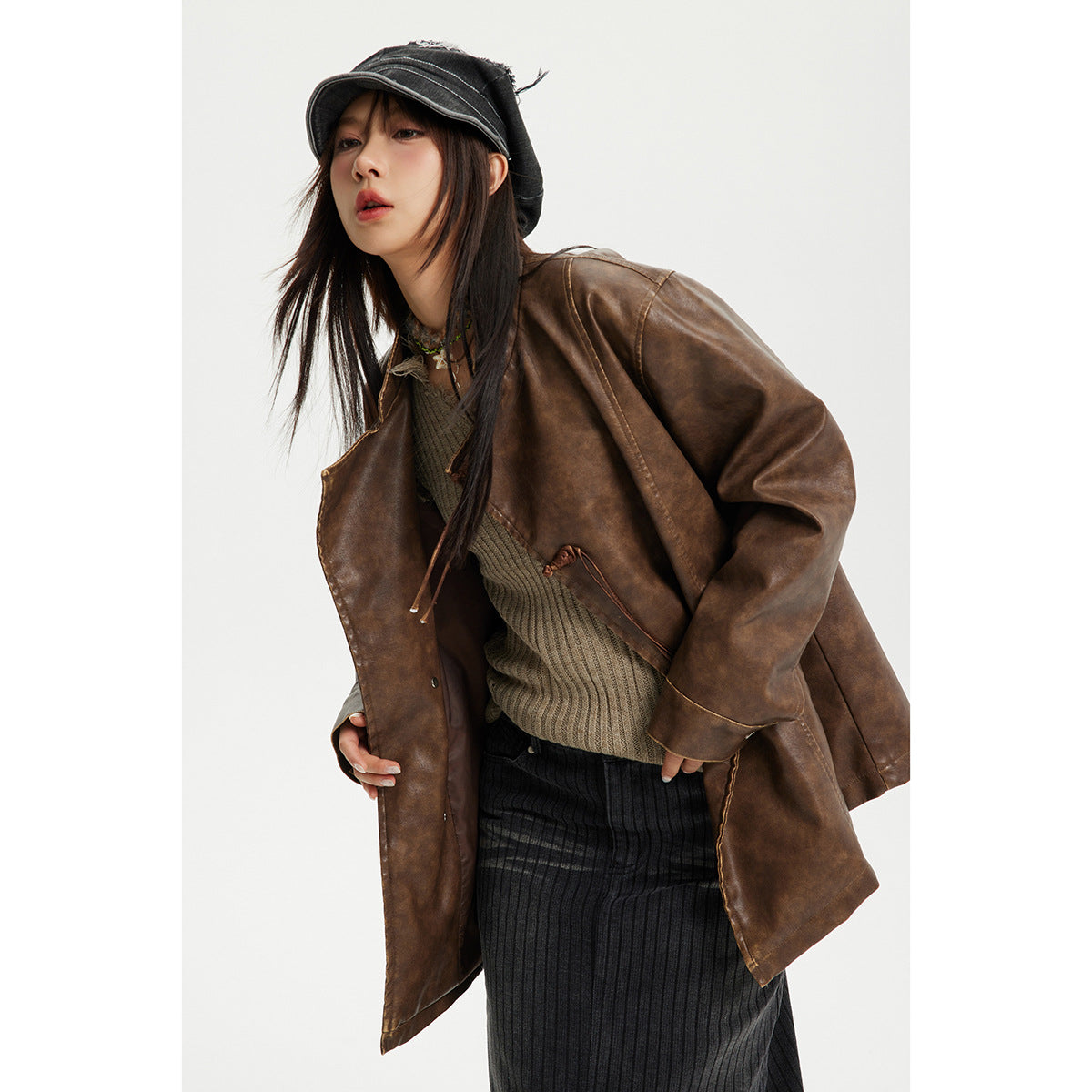 Model wears an open brown jacket with knotted cord closures over a knit top and dark skirt.