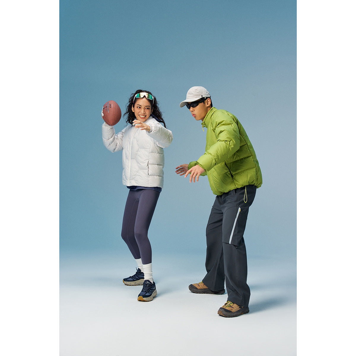 Two models in white and lime quilted jackets with dark pants, posing with a football against a blue backdrop.