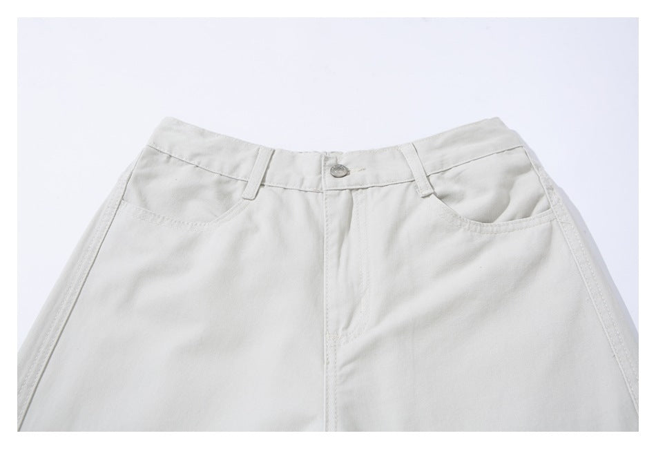 Close-up of the front waistband, button, belt loops, and curved pockets on ivory trousers.