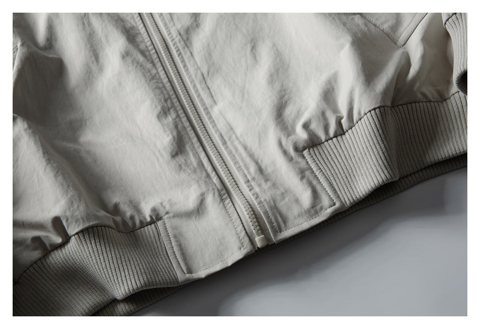 Close-up of a pale gray jacket's front zipper and rib-knit waistband.