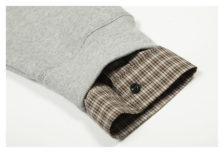 Close-up of a gray sweatshirt sleeve cuff layered over a brown plaid cuff with a black button.