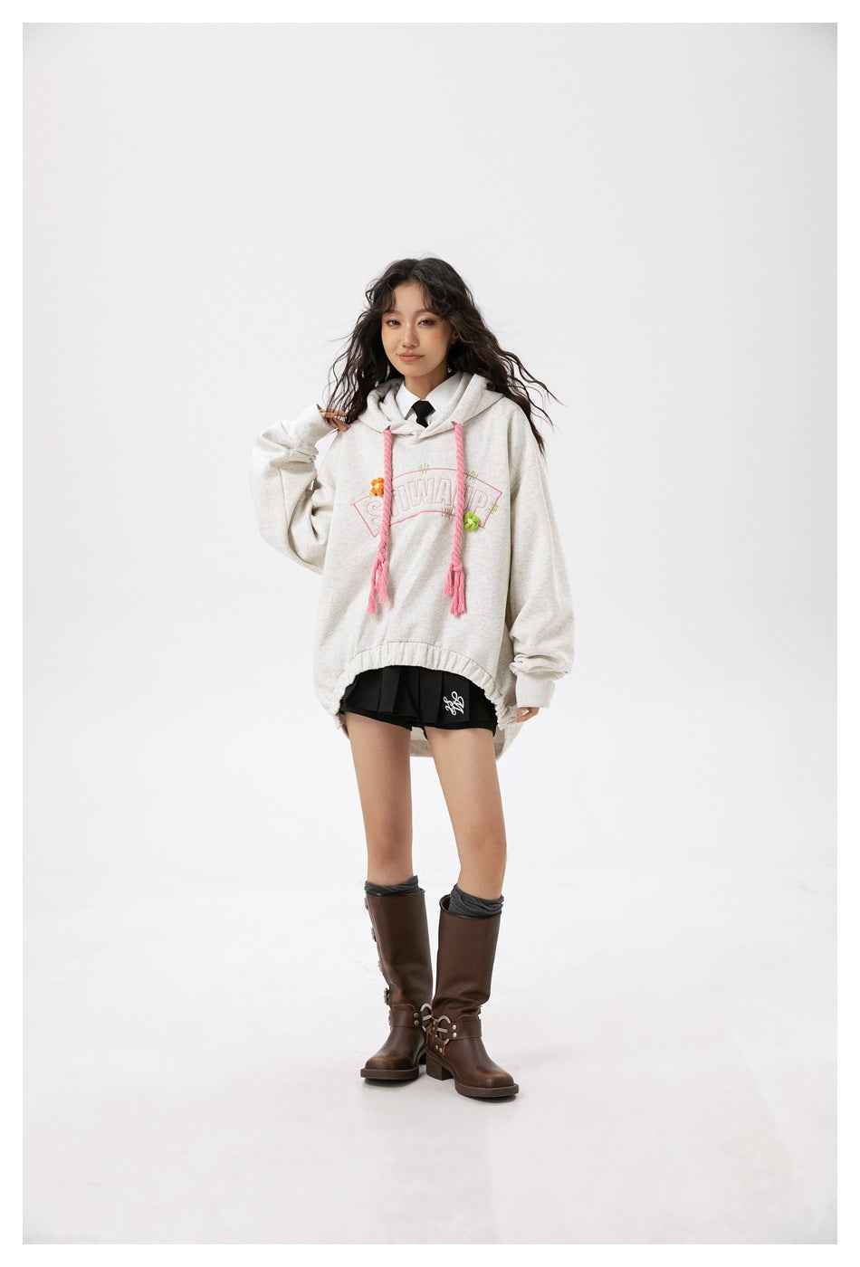 Model wearing an oversized light gray hoodie with pink braided drawstrings, black shorts and tall brown boots.