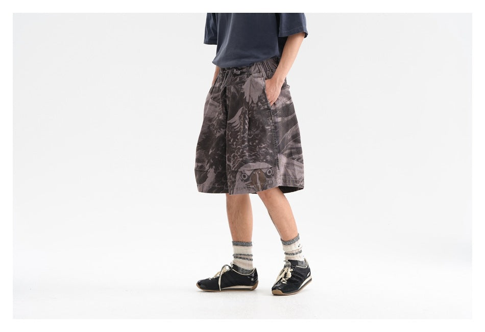 Front three-quarter view of a model wearing dark gray abstract-print shorts with a relaxed fit and side pockets.