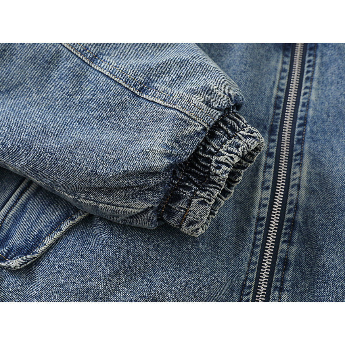 Close-up of the gathered elastic cuff and zipper on a blue denim jacket sleeve.