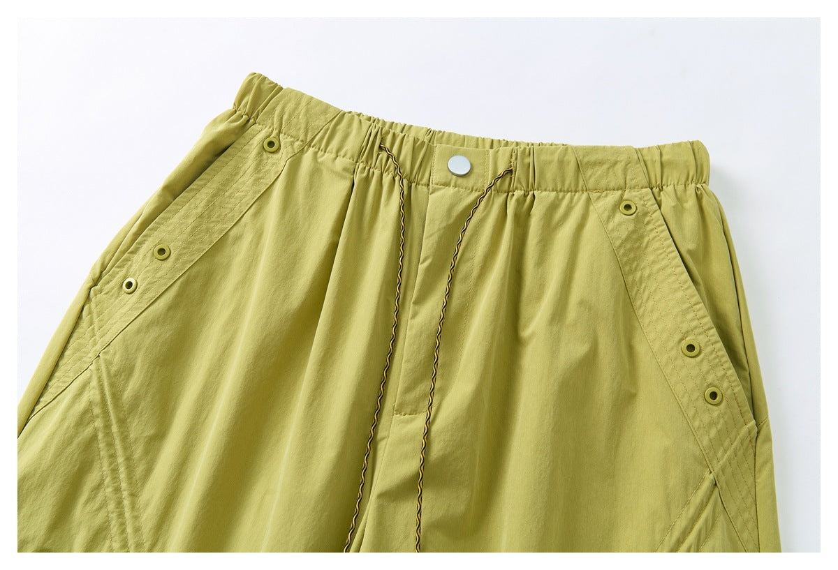 Close-up of the front waistband of mustard yellow-green trousers, with a snap closure, drawcords and buttoned side panels.