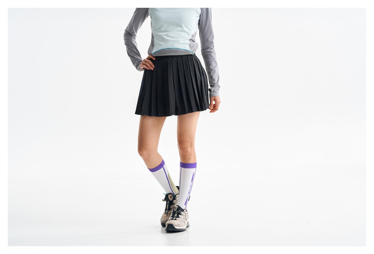 Cropped front view of a model wearing a black pleated athletic skirt and gray-and-pale-blue top.