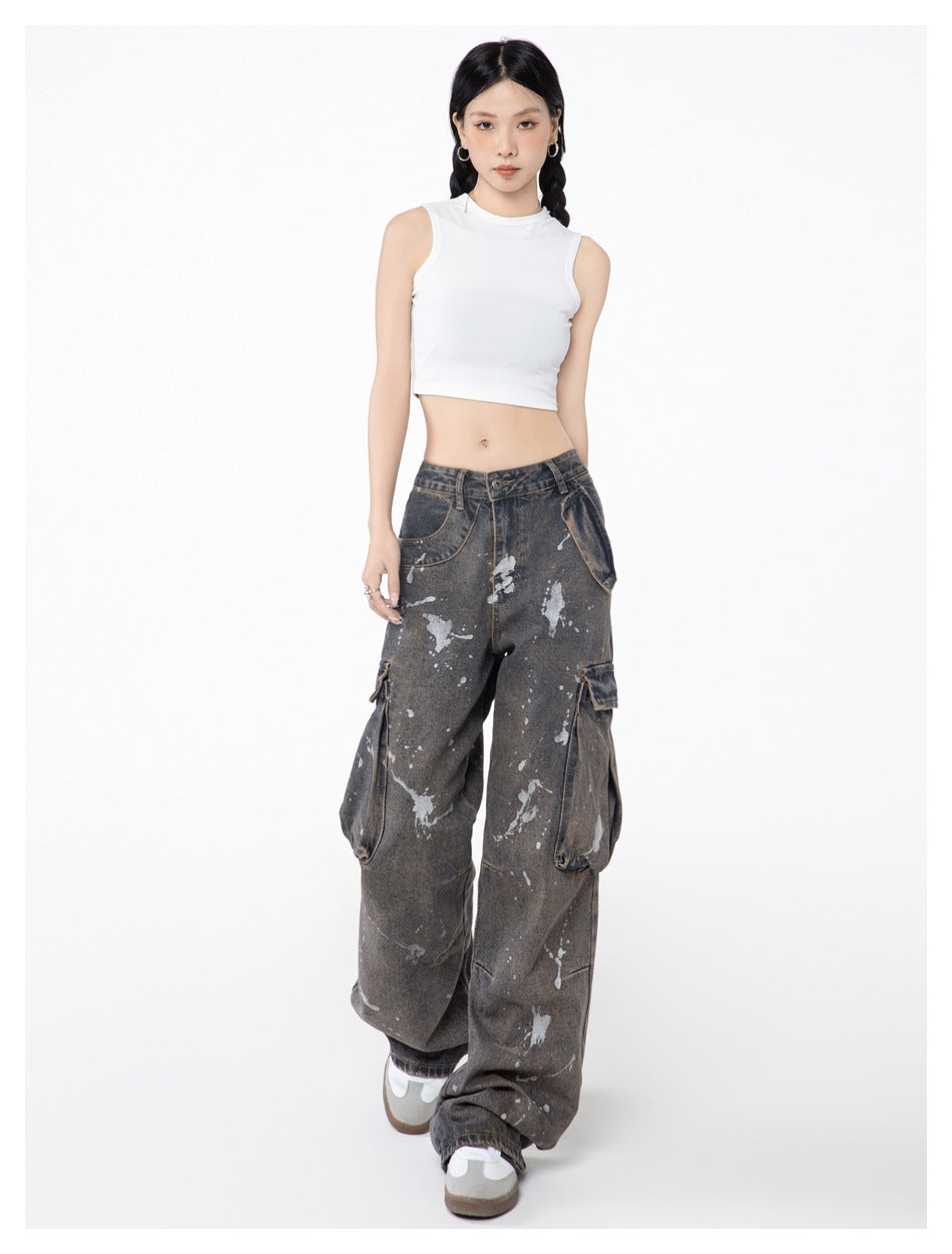 Full-length model wearing charcoal-gray paint-splatter cargo jeans with oversized pockets and a white cropped tank top.