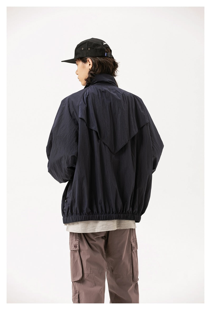 Rear view of a model wearing a dark navy jacket with a cape-like back flap and elastic hem, with mauve cargo pants.