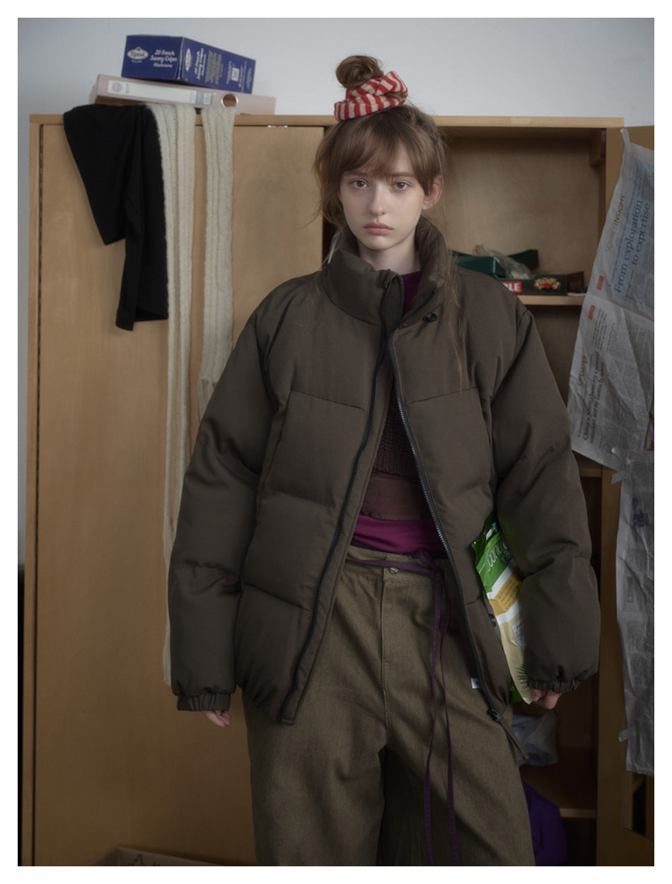 Model wearing an oversized dark brown puffer jacket with a high collar, zip front, and horizontal quilting.
