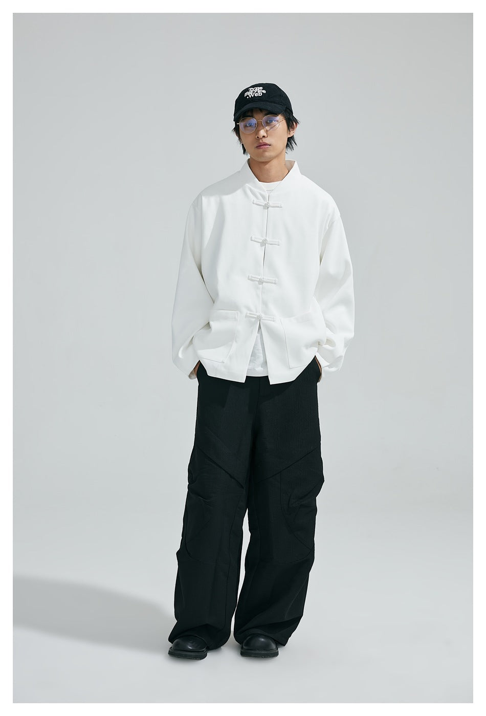 Model wearing the white frog-button stand-collar jacket with black wide-leg pants and a black cap