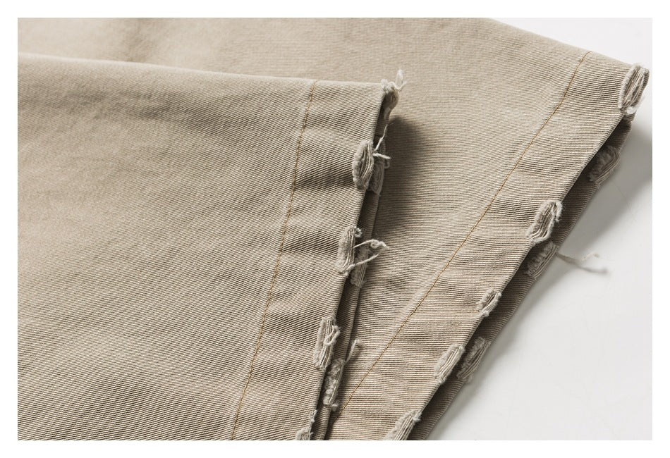 Close-up of beige twill trousers with frayed, distressed seams along the folded edge.