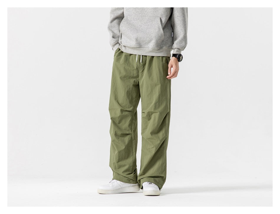 Front view of a model wearing loose olive-green pants with a drawstring waist and white sneakers.