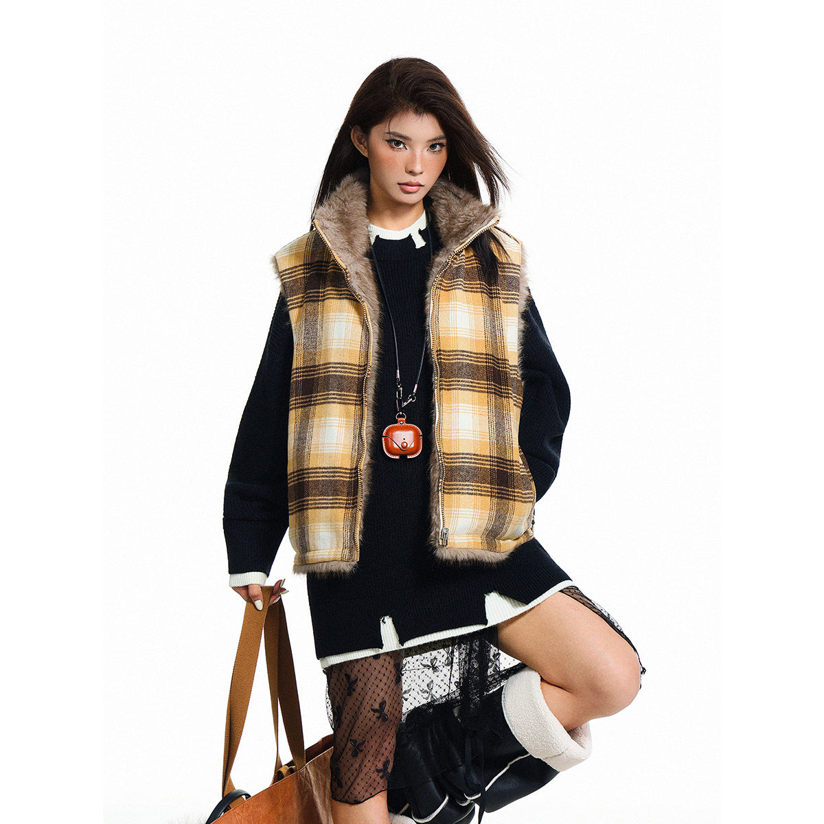 Model in a tan-and-black plaid zip vest with a fur collar, black sweater, sheer skirt and brown shoulder bag.