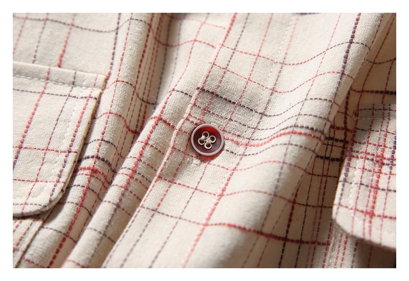 Close-up of a dark button and plaid fabric on the beige shirt, with part of a pocket visible.
