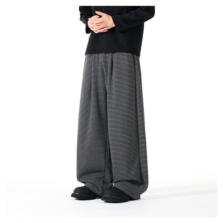 Front view of a model wearing loose black trousers with thin white horizontal stripes and a black top.