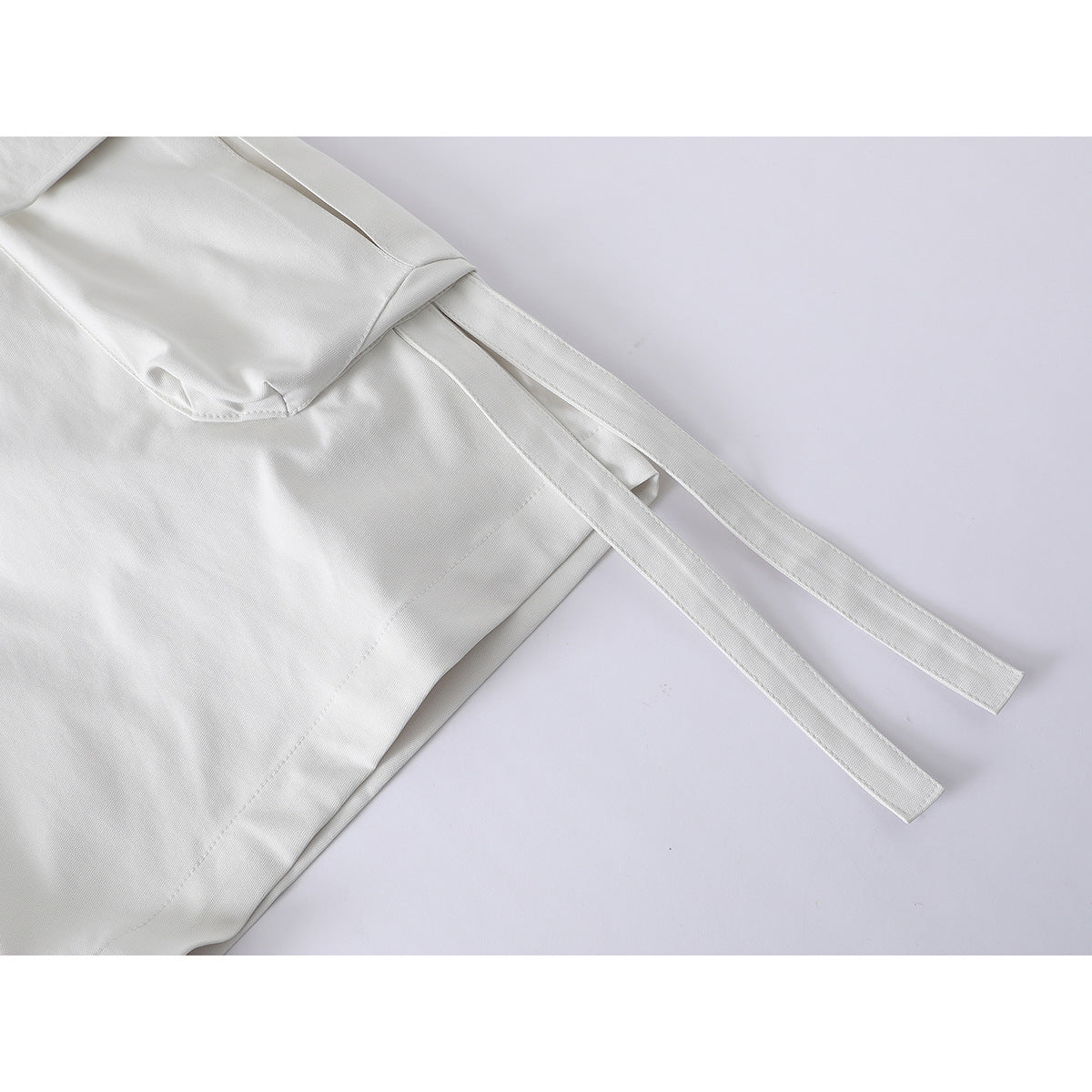Close-up of ivory shorts showing a large side pocket and two long fabric straps.