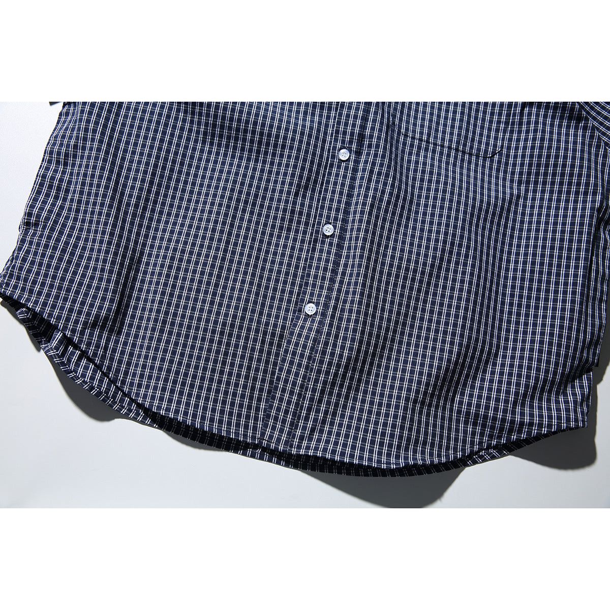 Close-up of the curved hem and button placket of a navy-and-white checked shirt.