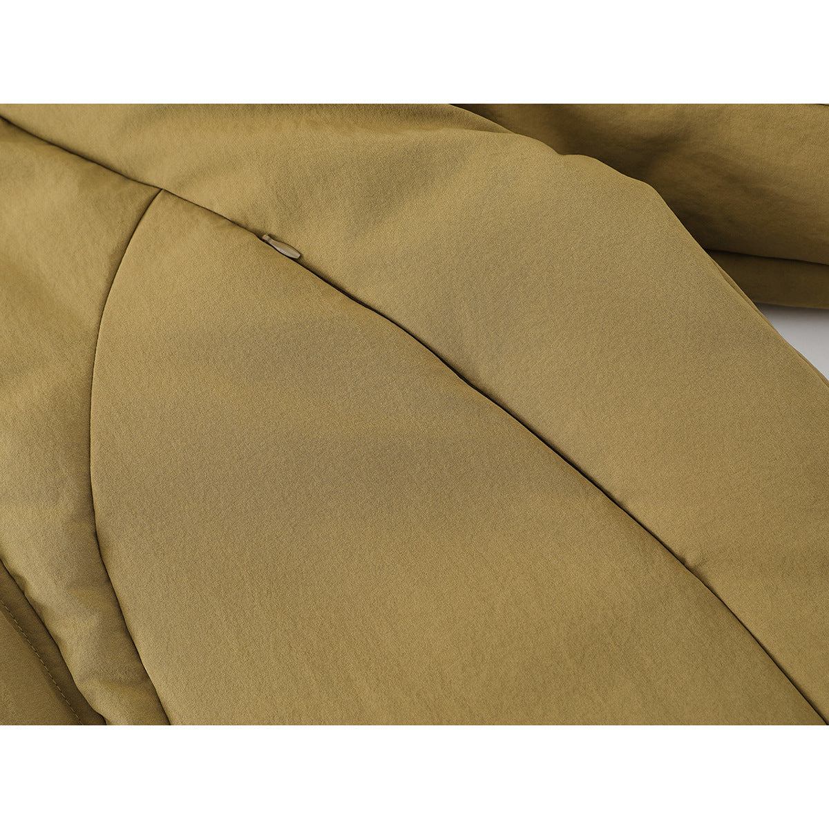 Close-up of tan jacket fabric and a small tab along a diagonal seam.