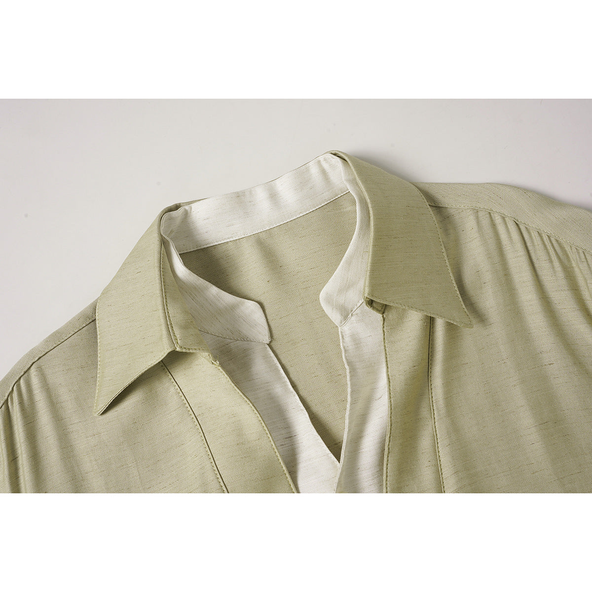 Close-up of a pale beige short-sleeve shirt with a pointed collar and contrasting light inner placket.