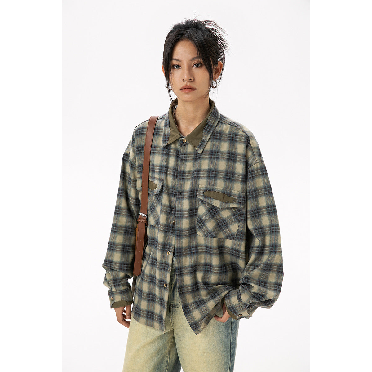 Model wearing a long olive and blue plaid shirt with distressed chest pockets, shown with loose faded jeans.