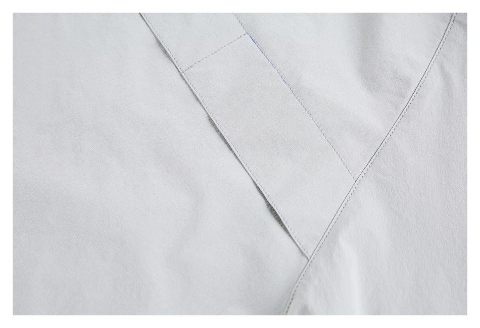 Close-up of pale gray garment fabric with a wide diagonal stitched panel or seam.