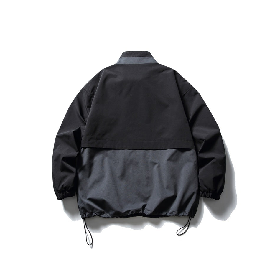 Back view of a black and charcoal color-block jacket with a flap across the upper back and hem cords.