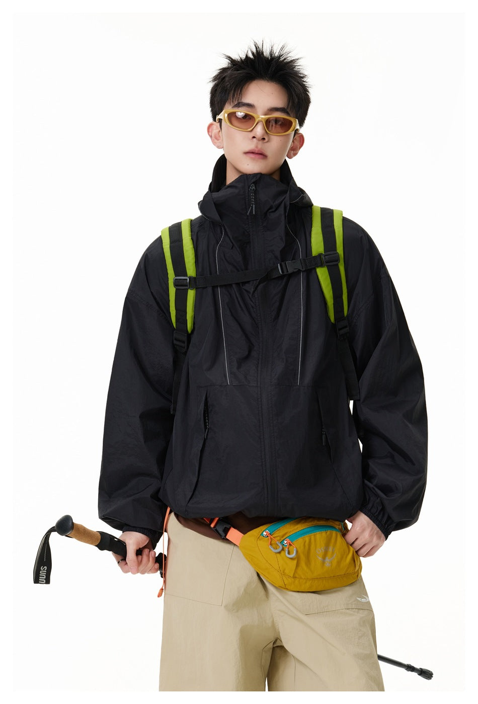 Closer front view of a model in a black zip jacket with a high collar and lime backpack straps.